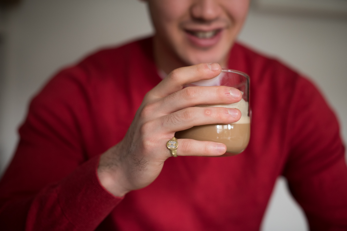 young man in red jumper with signet ring on pinky finger driking a cup of coffee, photograph by Fiona Bailey