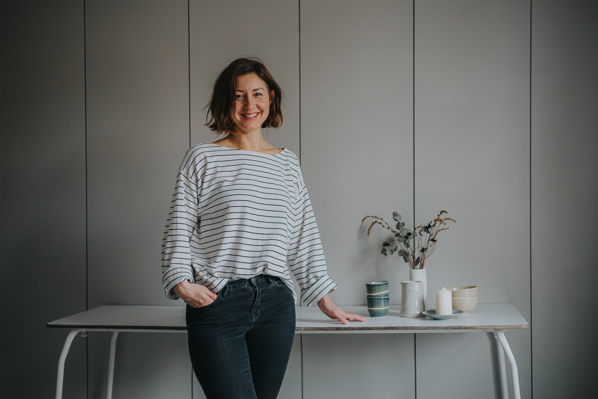 Emily Mathieson of Aerende — ethical interiors, life-improving homewares, Woman in striped shirt and jeans in front of table with homewares
